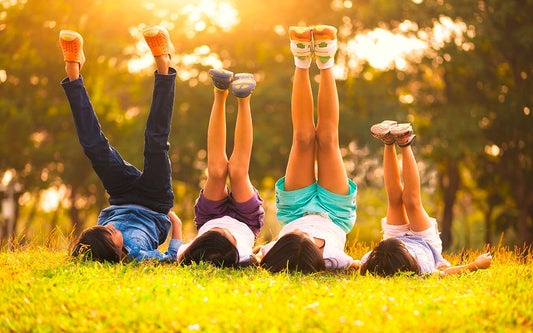 Mehrere Kinder liegen auf dem Rücken im Gras und strecken ihre Beine in die Luft. 
