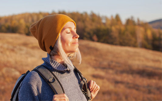 Person mit langen weißblonden Haaren und Mütze genießt Sonne beim Wandern