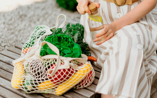 Frau mit Glasflasche und Zitronen und einer Einkaufstasche aus Stoff mit Obst und Gemüse gefüllt