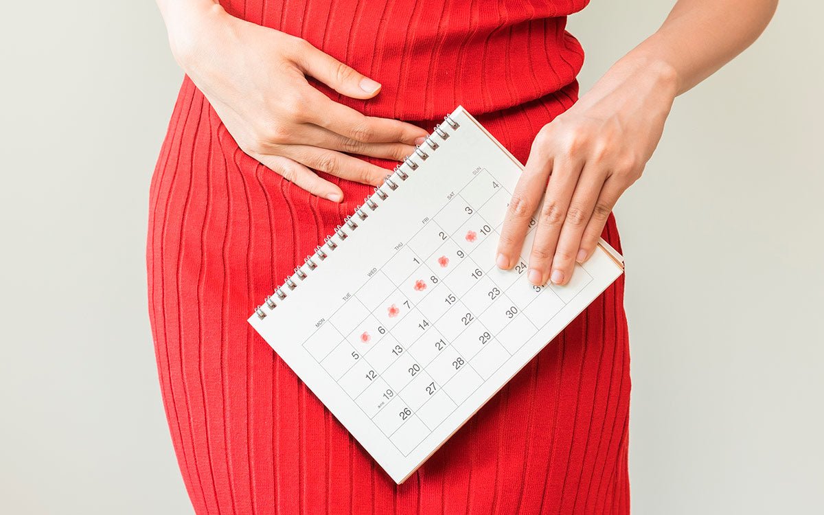 Person hält sich ihren Bauch und hält einen Zykluskalender in der anderen Hand